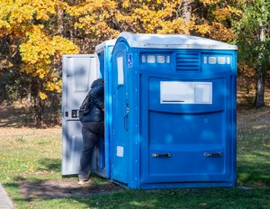 wheelchair accessible porta potty in a park next to a regular porta potty